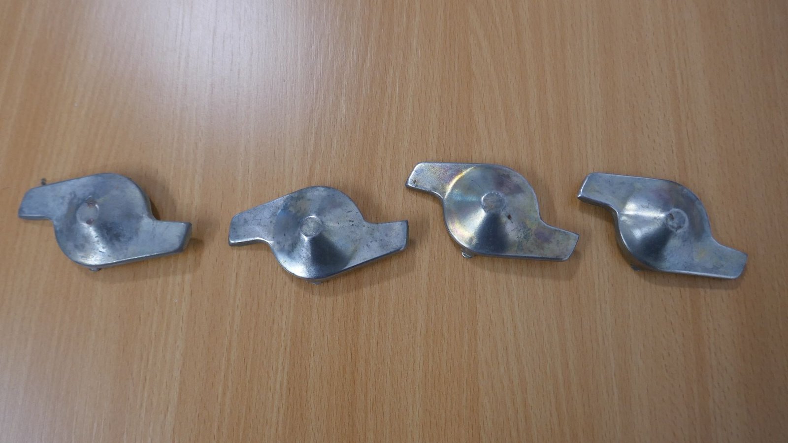 Auf einem Holztisch liegen vier Metallteile.